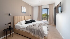 A modern bedroom with a large bed, a small side table with a vase, a painting on the wall, and a TV mounted on the wall. - Villa Kalea With Pool (Labin)