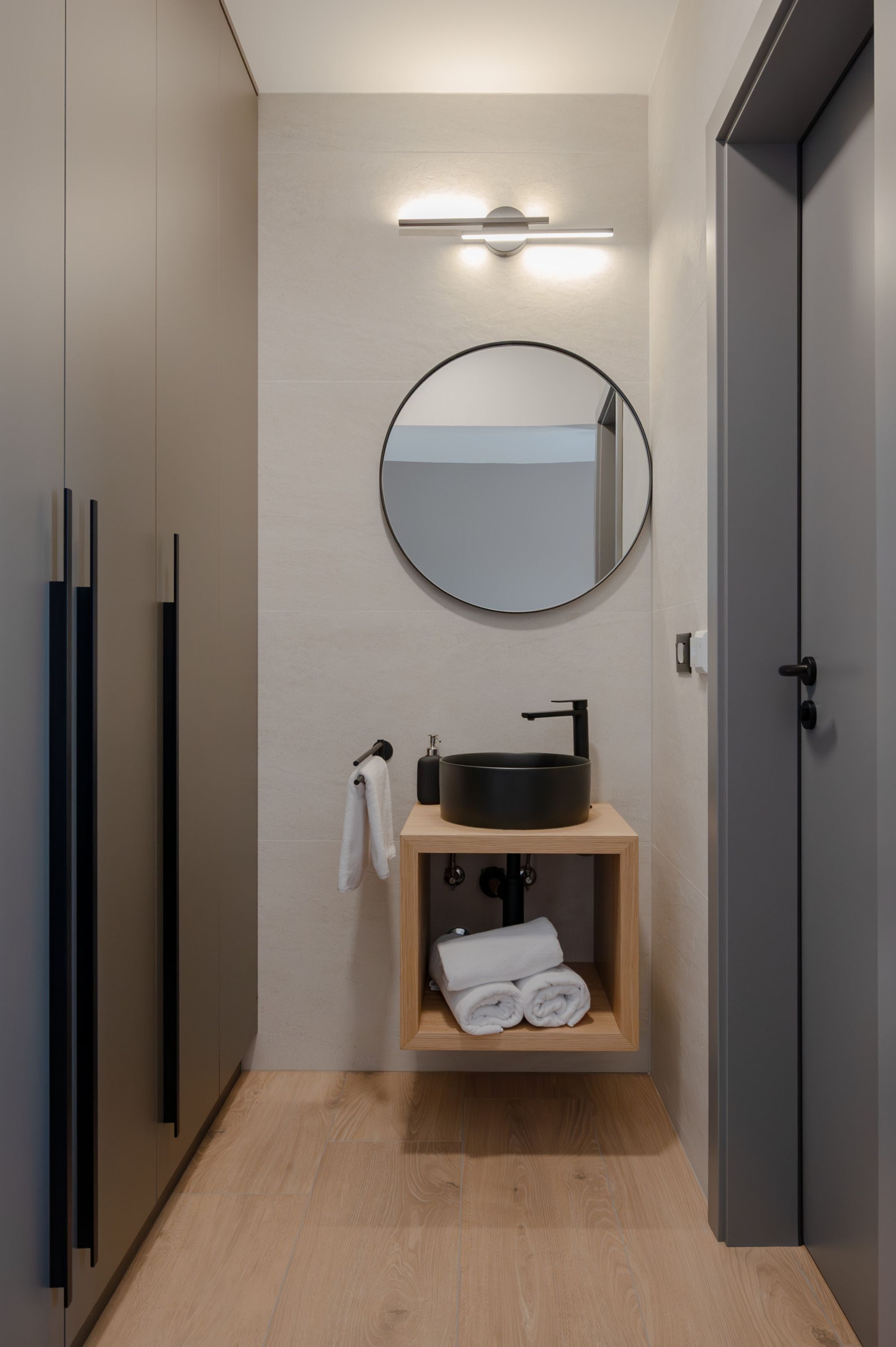 A modern bathroom with a wooden vanity, a round mirror, and a towel rack.