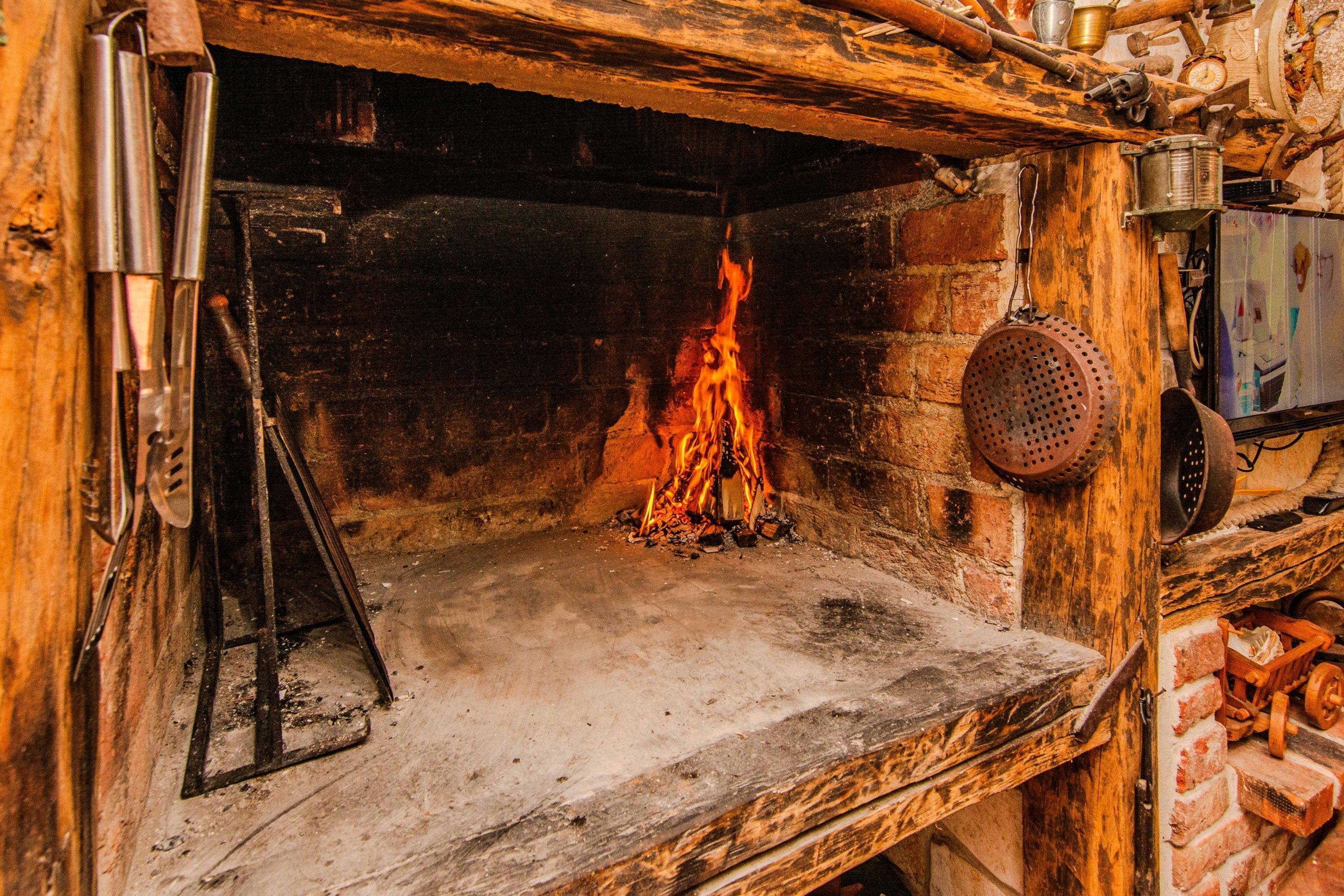 Una chimenea de piedra rústica con fuego encendido, rodeada de vigas de madera y paredes de ladrillo.