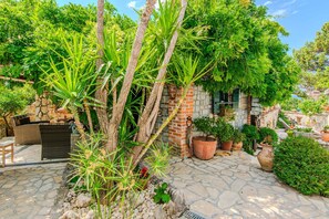 Un patio in pietra con vasi di piante, un divano in vimini e un muro in mattoni con una pianta pensile.
