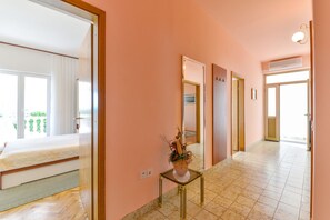 A hotel hallway with a bed in the left room, a small table with a plant, and a door leading to another room. - Beachfront Apartment Liveri 2 (Vir)
