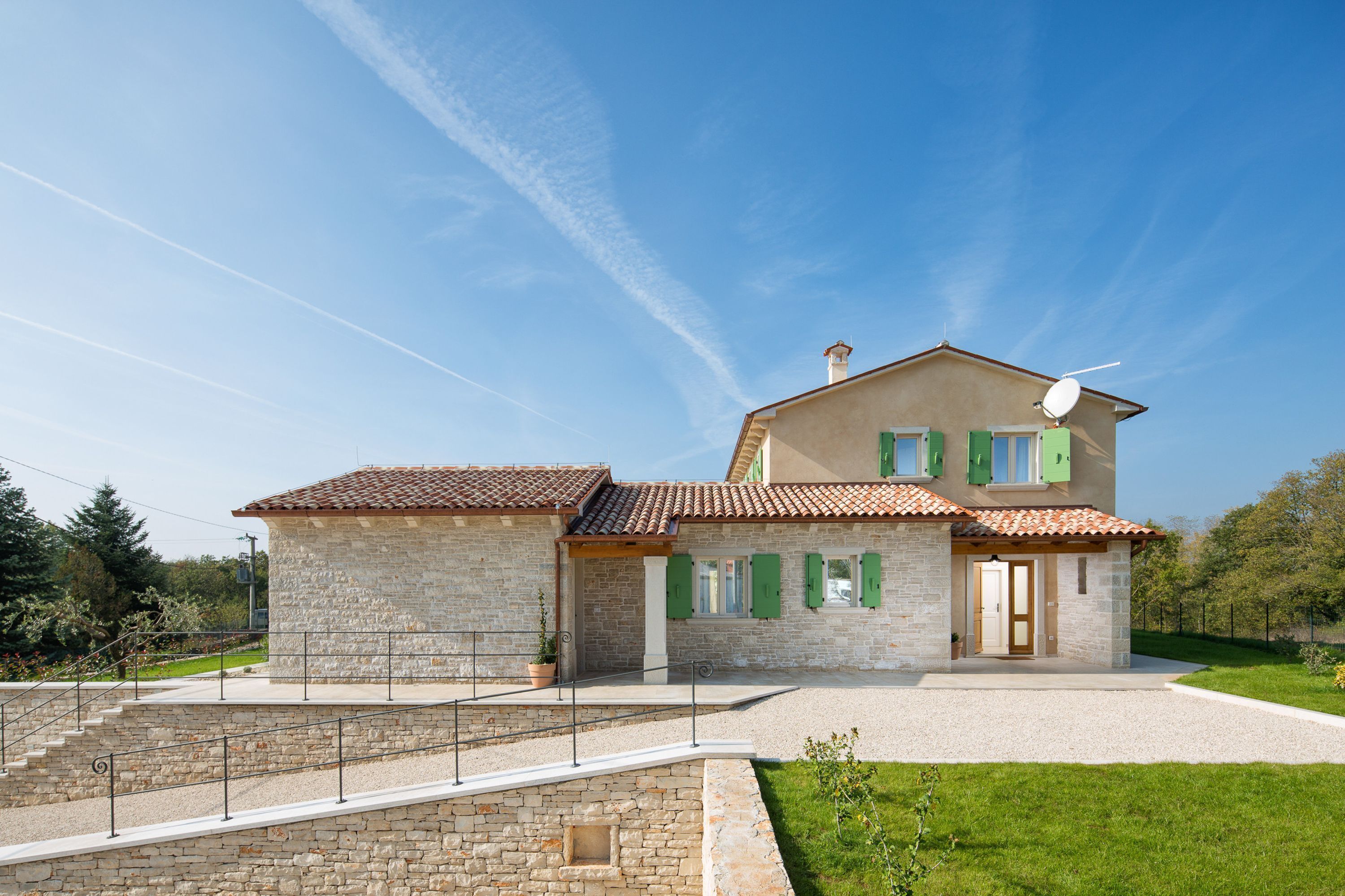 A two-story stone house with a tiled roof, green shutters, and a satellite dish.