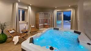 Ein moderner Wellnessbereich mit Whirlpool, Holzliegen und Blick ins Freie.