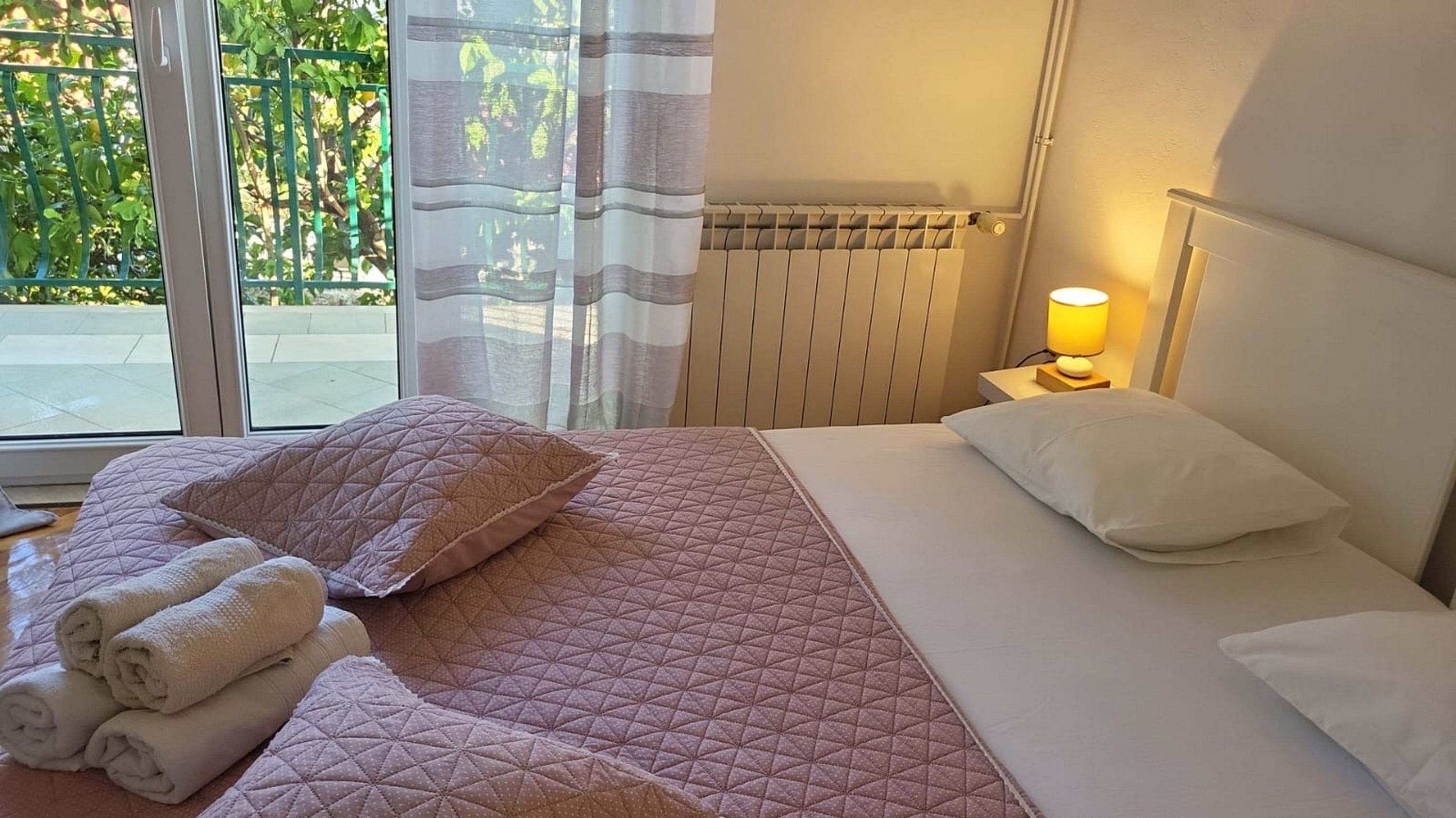 Una camera d'hotel con un letto, un comodino con una lampada, una finestra con tende e vista sul verde.