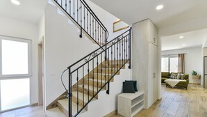 A staircase with wooden steps and black railings, leading to a landing with a white bench and a green sofa in a well-lit room with wooden flooring. - Villa Rea 4 With Heated Pool (Privlaka)