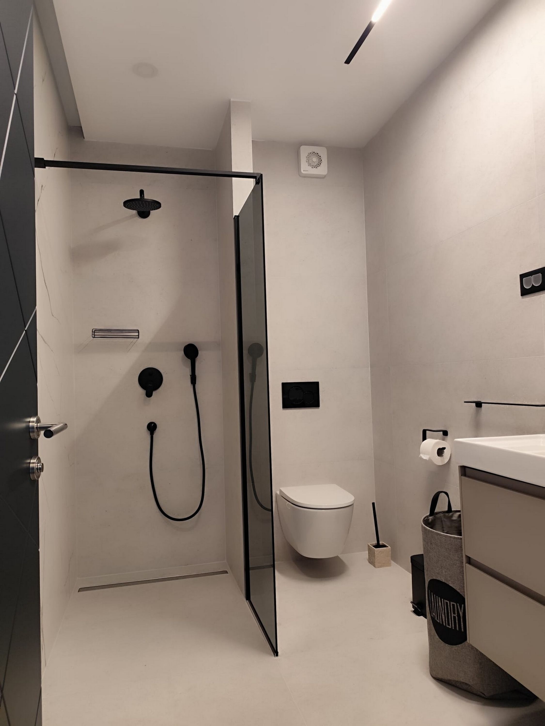 Et moderne badeværelse med et glasafskærmet brusebad, toilet og håndvask med håndklædestang.
