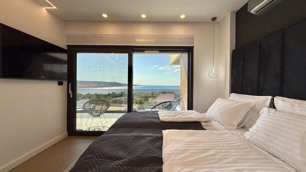 Un dormitorio moderno con una cama grande, un televisor montado en la pared y un balcón con vistas al paisaje.