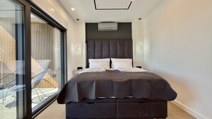 Un dormitorio moderno con una cama grande, un ventanal que da a un balcón y un equipo de aire acondicionado en la pared.