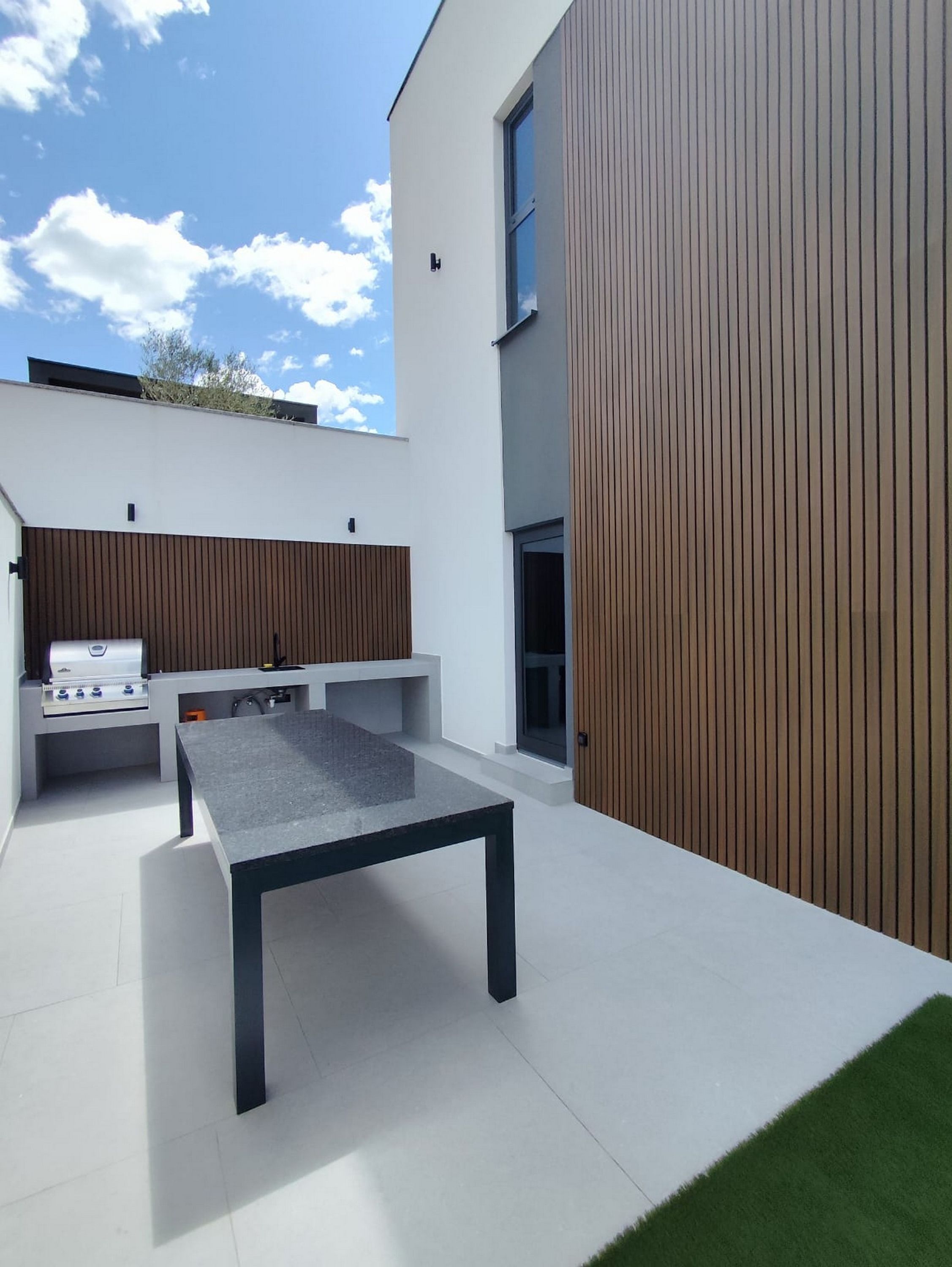 Ein moderner Außenbereich mit Küche, inklusive Grill, Tisch und integriertem Sitzplatz.