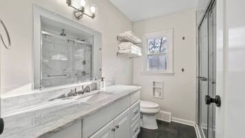 A modern bathroom with a large mirror, a sink with a marble countertop, a toilet, and a glass shower enclosure.