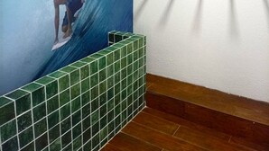 A bathroom with a large mural of a surfer on a wave, green tiled walls, and a wooden floor. - Mahrak Villa - Porto de Galinhas (Ipojuca)