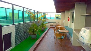 A rooftop terrace with a view of the sea, potted plants, wicker chairs, and a barbecue grill. - Mahrak Villa - Porto de Galinhas (Ipojuca)