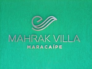 Ein Logo mit dem Text "MAHRAK VILLA MARACAÍPE" vor einem strukturierten grünen Hintergrund.