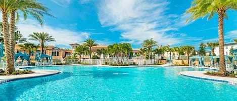 A swimming pool with palm trees and lounge chairs, surrounded by buildings with a clear sky.