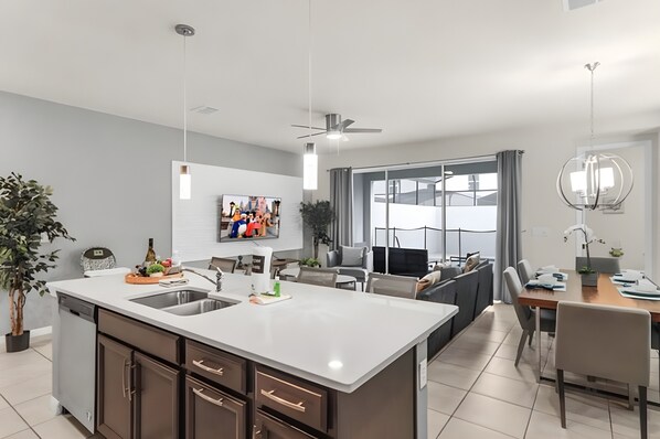 A modern kitchen with a central island, built-in appliances, and a dining area with a large window. - Family 5BR Home with Pool at Solara (Kissimmee)
