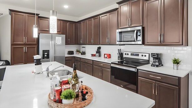 Cozinha moderna com armários marrons, eletrodomésticos de aço inoxidável e uma ilha central com diversos objetos.