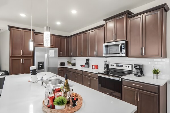 A modern kitchen with brown cabinets, stainless steel appliances, and a central island with various items. - Family 5BR Home with Pool at Solara (Kissimmee)