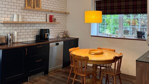 Eine Küche mit einem Holztisch und Stühlen, einer Kaffeemaschine und einem Fenster mit Blick auf Grünflächen.