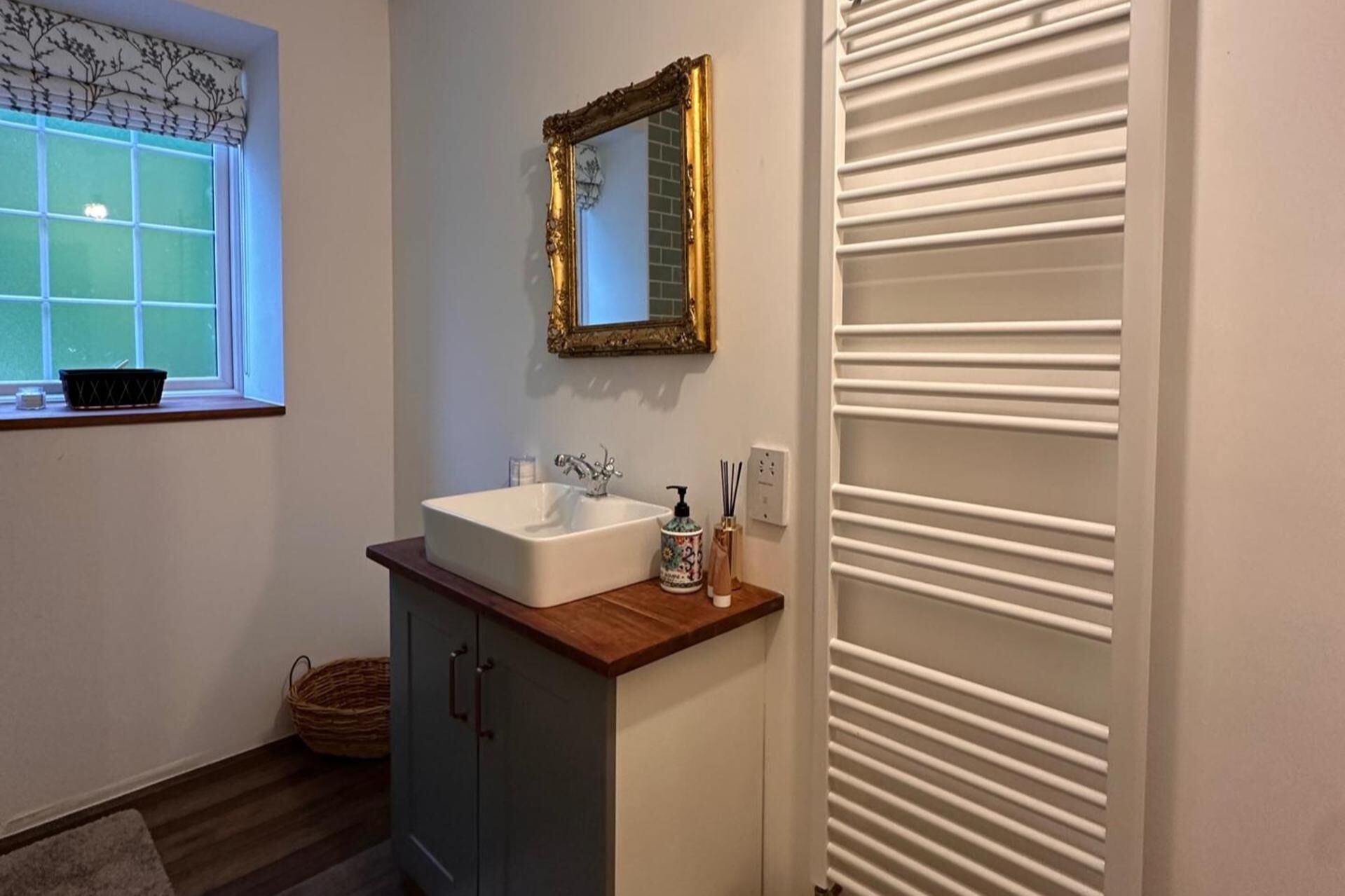A bathroom with a white sink, a decorative mirror, and a window with a view of greenery.