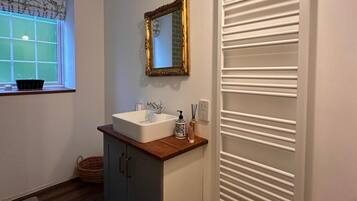 A bathroom with a white sink, a decorative mirror, and a window with a view of greenery.