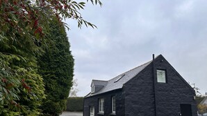 Ein schwarzes Steinhaus mit steilem Dach, einem kleinen Fenster und einer Tür.