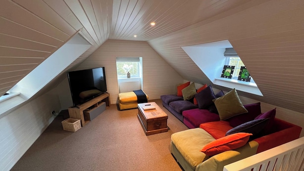 Ein gemütliches Dachwohnzimmer mit Fernseher, einer Couch, einem Couchtisch und einem Fenster mit Dekoration.