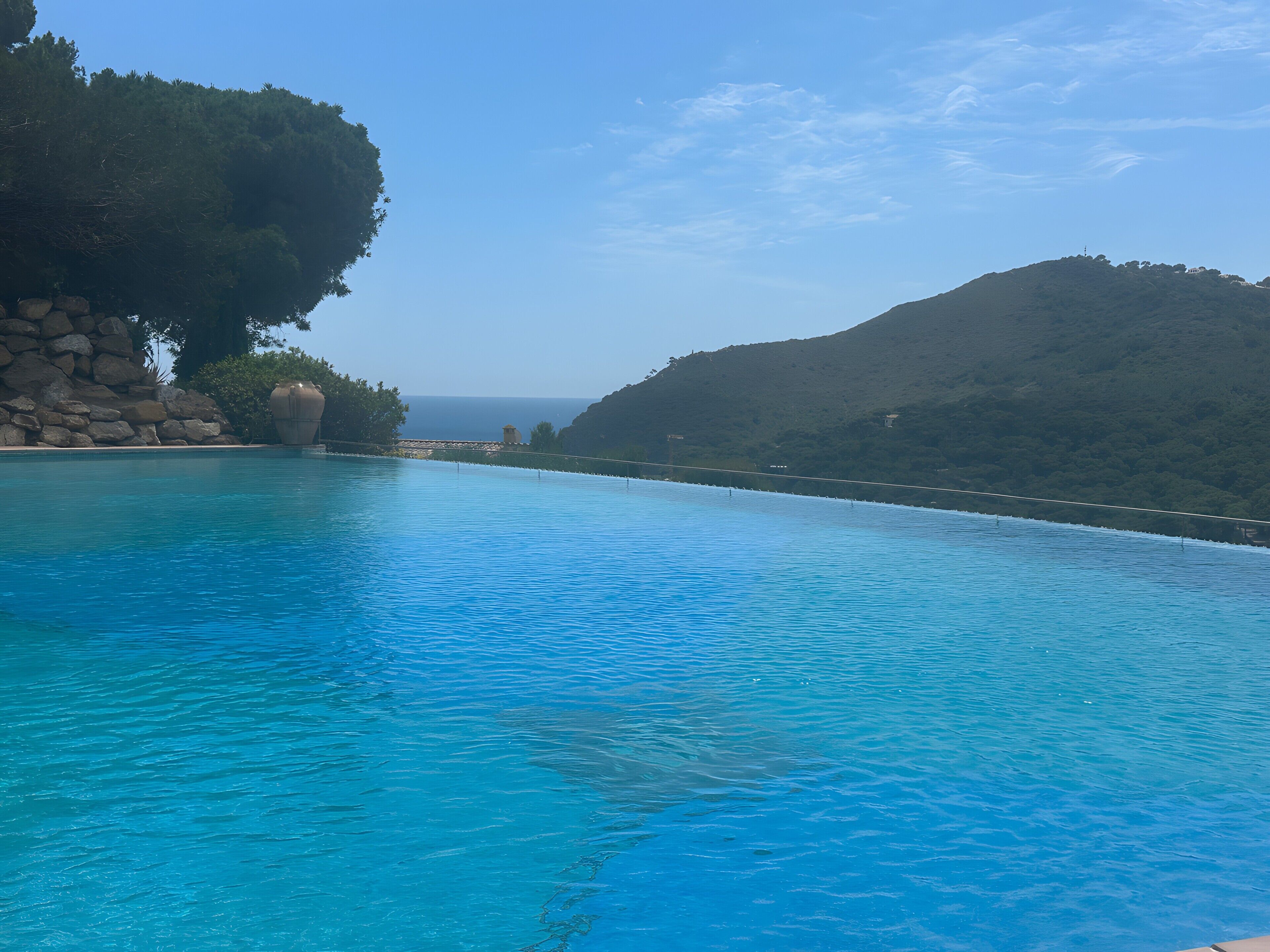 Ein klares, blaues Schwimmbecken mit Blick auf das Meer und die Hügel.