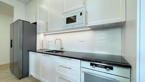Une cuisine moderne avec des meubles blancs, un réfrigérateur en acier inoxydable, un four encastré et un four à micro-ondes.