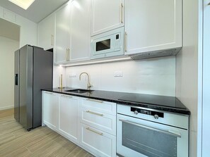 Eine moderne Küche mit weißen Schränken, einem Edelstahl-Kühlschrank, einem Einbauofen und einer Mikrowelle.