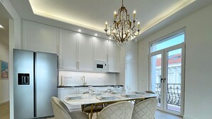 Une cuisine moderne avec des meubles blancs, un réfrigérateur en acier inoxydable, un lustre et un coin repas avec une table dressée pour quatre personnes.