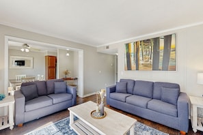 A living room with two grey sofas, a coffee table, and a painting on the wall. - Condo in oceanfront building w/ pools, hot tubs, arcade, & beach access (Myrtle Beach)