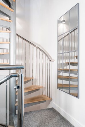 A modern staircase with wooden steps and metal railings, leading to a landing with a glass partition.
