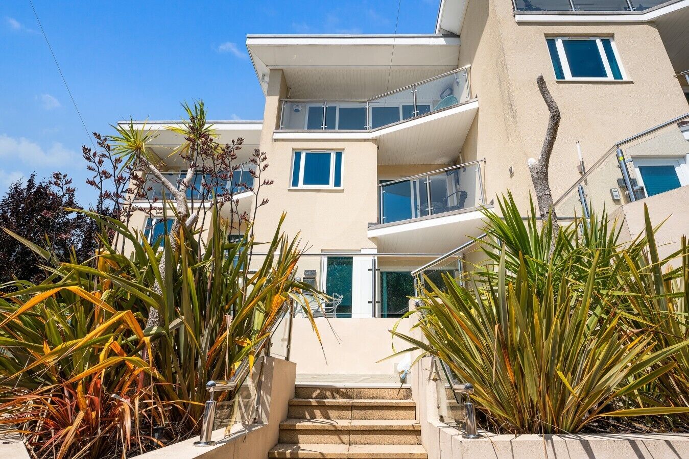 Un immeuble à plusieurs étages doté de balcons, d’un escalier et de plantes tropicales.