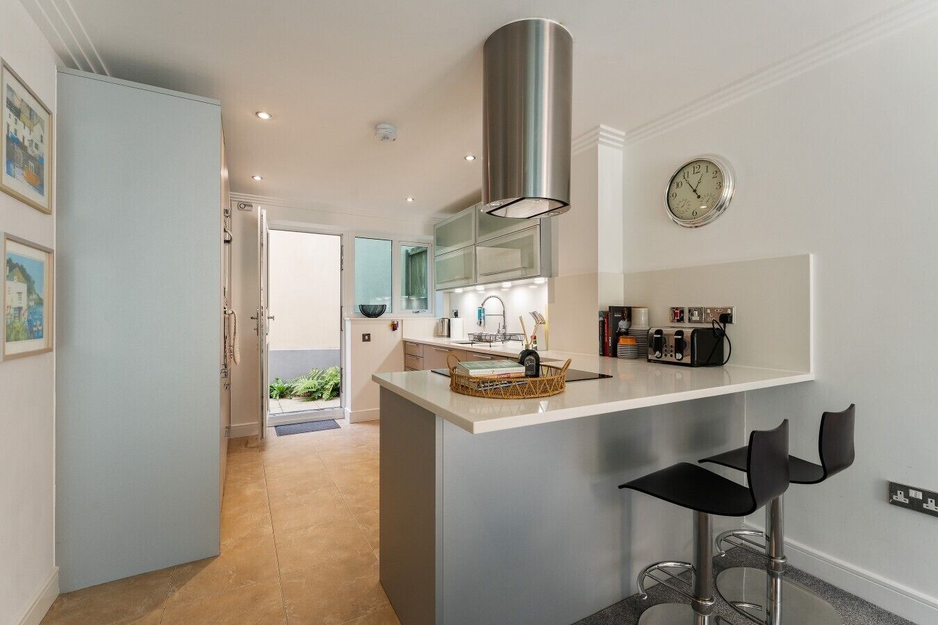 A modern kitchen with a central island, stainless steel appliances, and a visible clock.