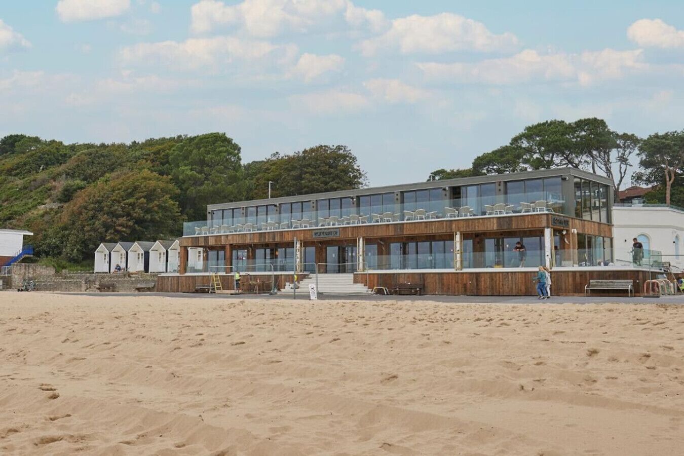 A modern beachside building with multiple levels, large windows, and a wooden facade.