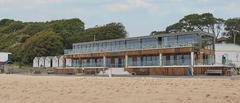 A modern beachside building with multiple levels, large windows, and a wooden facade.