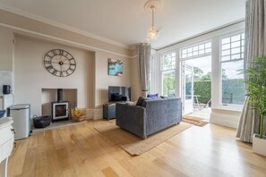 A spacious living room with a large window, a fireplace, a sofa, and a television. - Pinewood Retreat - Garden Apartment Close To Beach (Branksome Park)
