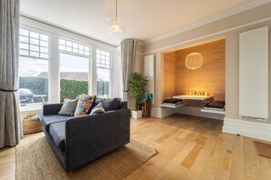 A modern living room with a grey sofa, a wooden accent wall, and a large window. - Pinewood Retreat - Garden Apartment Close To Beach (Branksome Park)