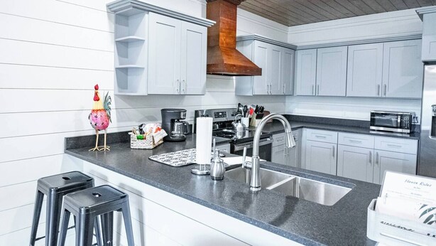 Een moderne keuken met witte kastjes, een RVS-spoelbak, een koffiezetapparaat en een magnetron.