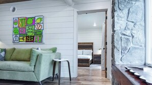 Een moderne woonkamer met een groene bank, een klein rond tafeltje en een kleurrijk abstract schilderij aan de muur.
