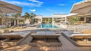 Ein Poolbereich mit Liegestühlen, Sonnenschirmen und blauem Himmel.
