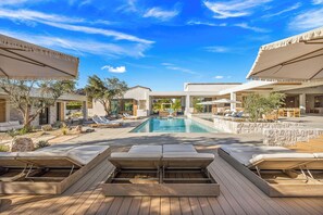 Ein Poolbereich mit Liegestühlen, Sonnenschirmen und blauem Himmel.