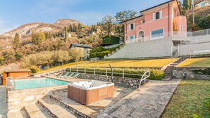 A pool area with a hot tub, stone steps, and a view of a hillside with buildings. - Villa La Perledina in Perledo (Perledo)