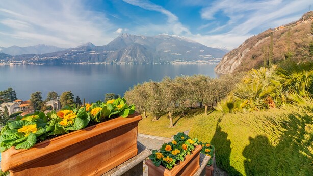A scenic view of a lake with mountains in the background, a balcony with flower planters, and a clear sky. - Villa La Perledina in Perledo (Perledo)