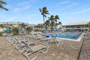 A pool area with lounge chairs and umbrellas, surrounded by palm trees and buildings. - La Palma Verde at Outdoor Resorts (Layton)