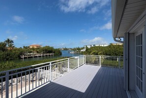 A wooden deck with a white railing overlooking a calm body of water, surrounded by greenery and buildings. - Sombrero Sands 3/2 w pool + 80 ft dock, .5 miles to Sombrero Beach (Marathon)