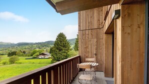 A wooden balcony with a view of a green landscape and a house in the distance.