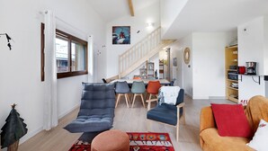 A modern living room with a sofa, chairs, a coffee table, and a staircase leading to a dining area.