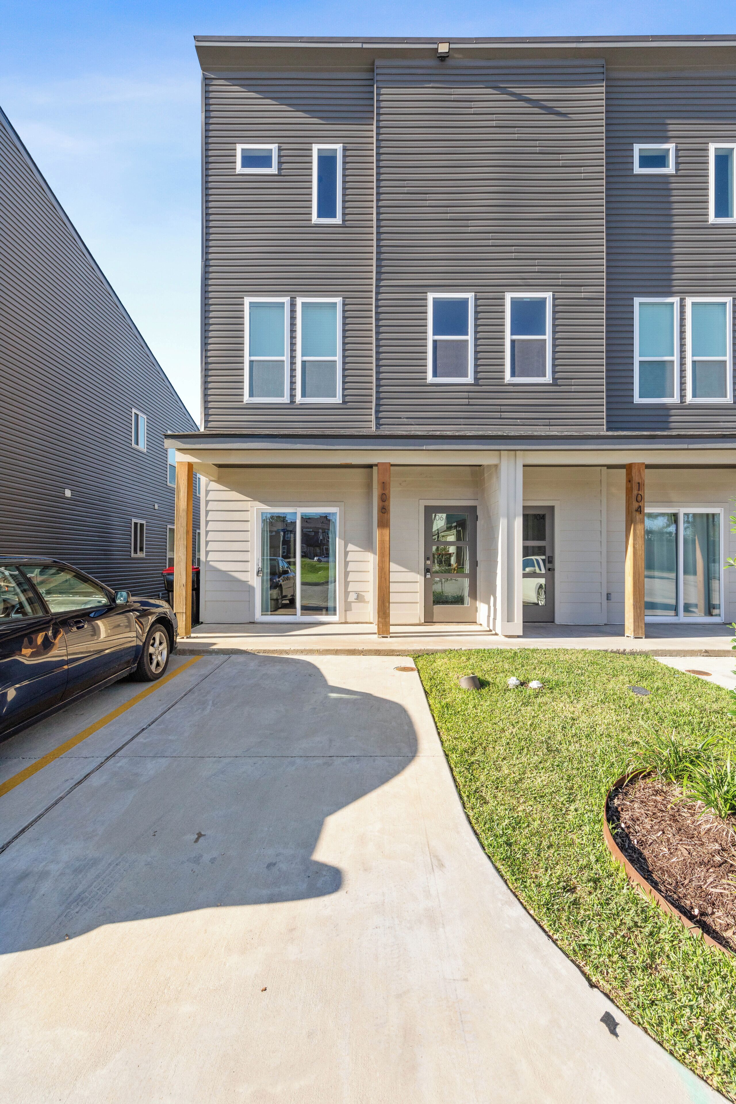 A multi-story residential building with a driveway, a parking area, and a well-maintained lawn.