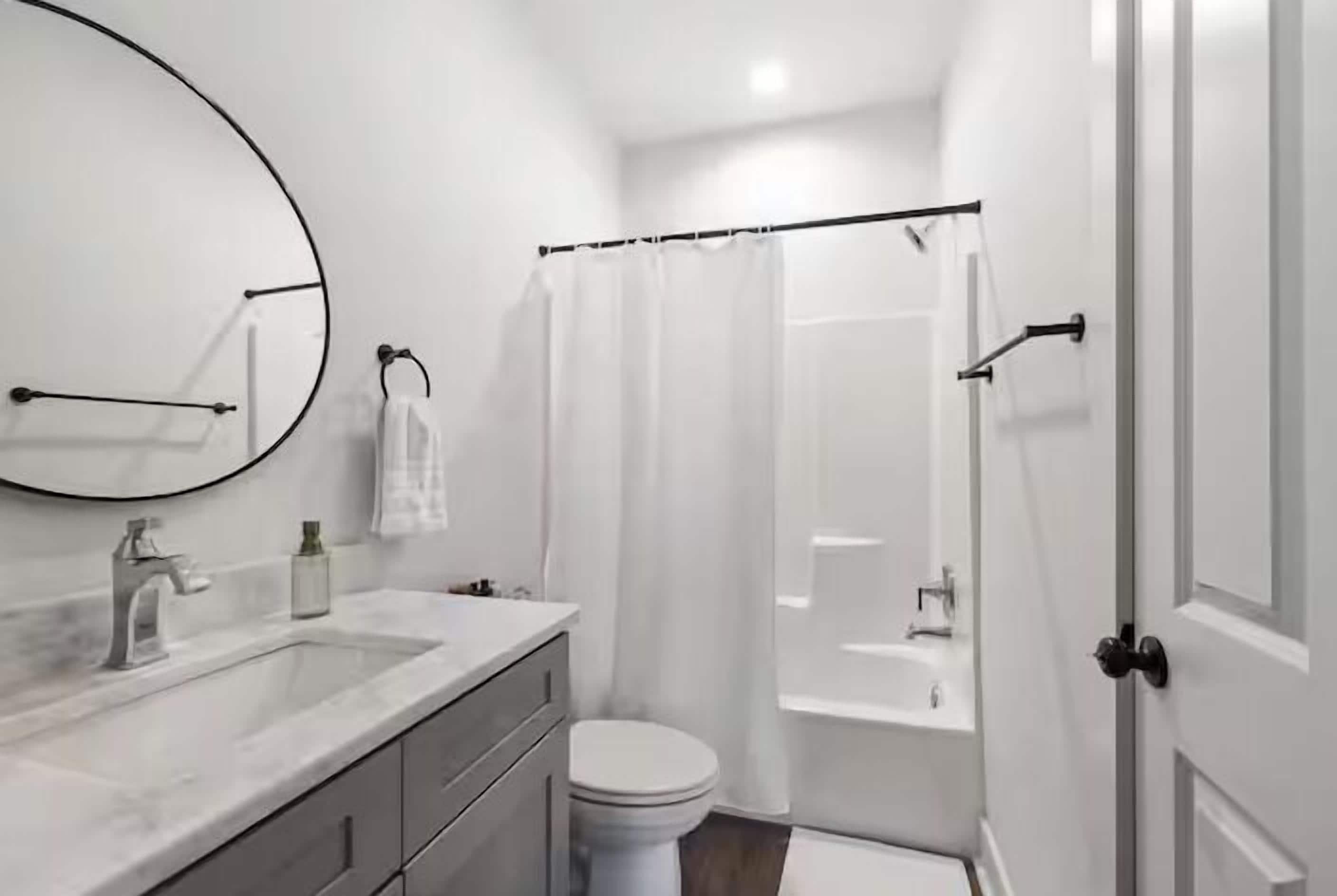 A modern bathroom with a white sink, mirror, toilet, and shower area.